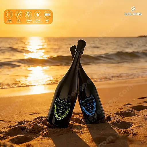 Dos botellas de champán oscuro con etiquetas de escudo verde y azul se apoyan juntas en la arena de una playa al atardecer, con el océano y el sol poniente brillando en el fondo.
